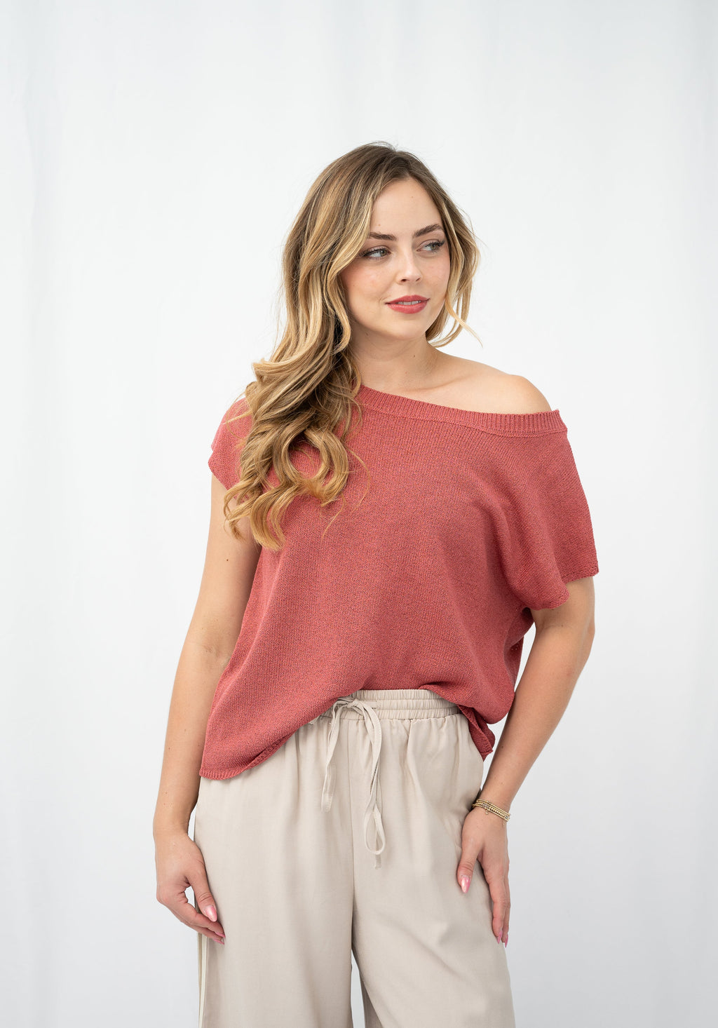 Model wearing a crepe yarn knit top with an off-shoulder design and light beige trousers.