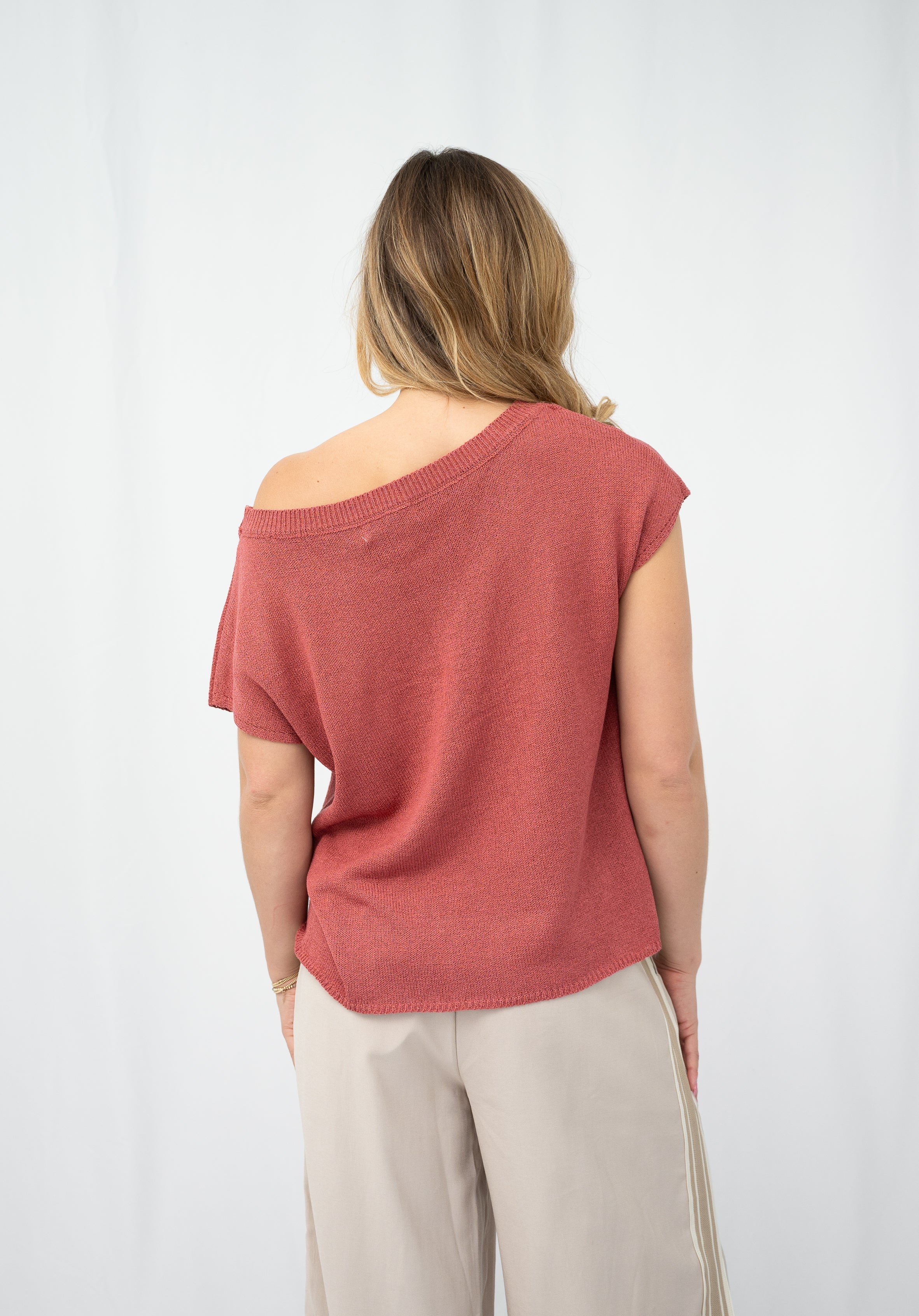 Back view of a woman wearing a crepe yarn knit top in coral, showcasing its relaxed fit and short sleeves.