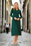 Model wearing the Ckm Zoe Dress, a green midi dress with a high neck and zip closure, strolling in a city street.