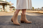 Kansley Boot in tan worn by a woman standing on a gravel road, showcasing its chic Chelsea silhouette.
