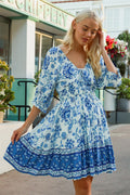 Model wearing the Catherine Mini Dress with blue patterns and peasant sleeves outside a shop.