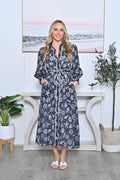 Model wearing Starfish Dress, a maxi-length dress with long sleeves, tie belt, and pockets, featuring a navy base with white print.