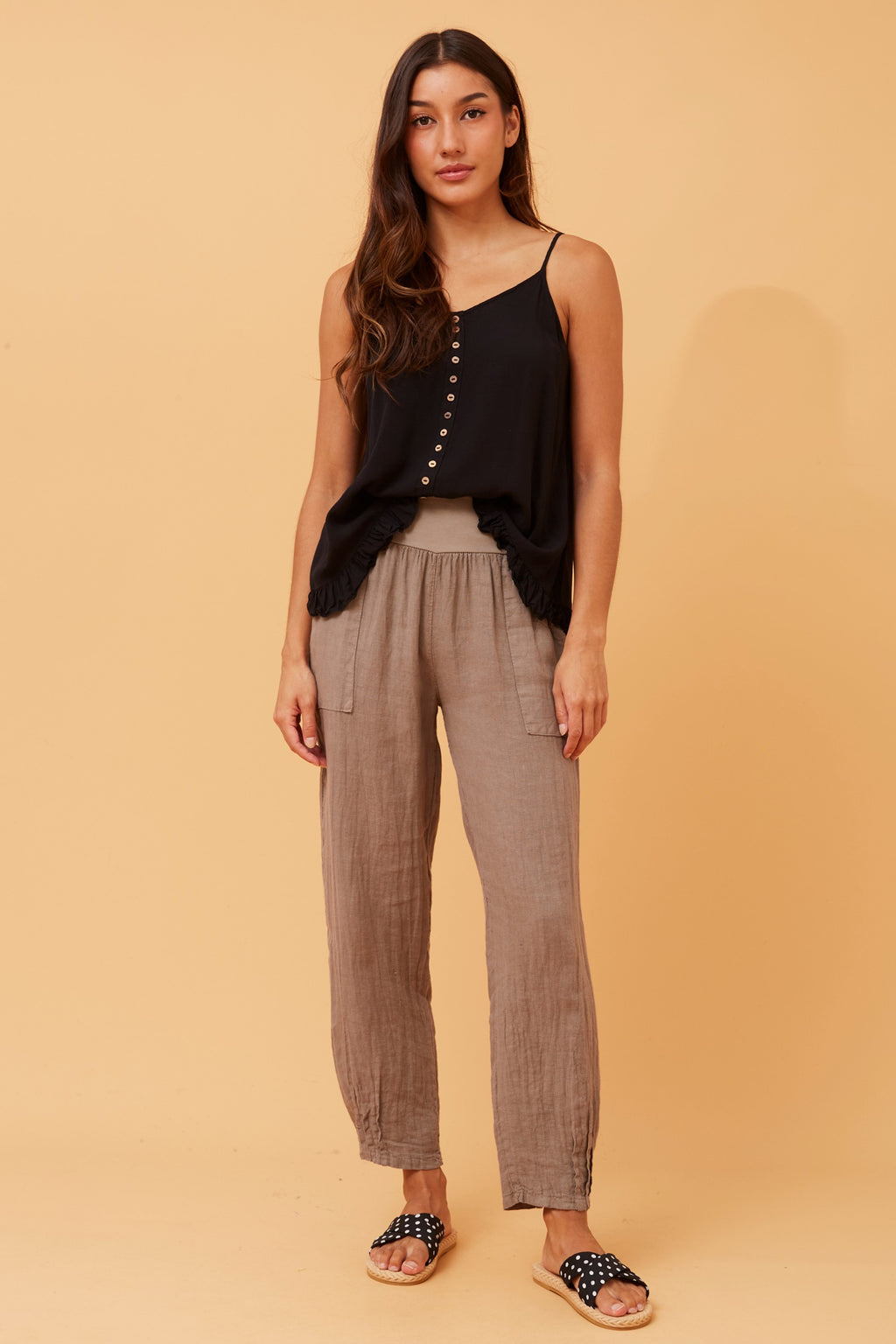 Model showcasing Roma Linen Pants with a stylish black tank top against a warm background.