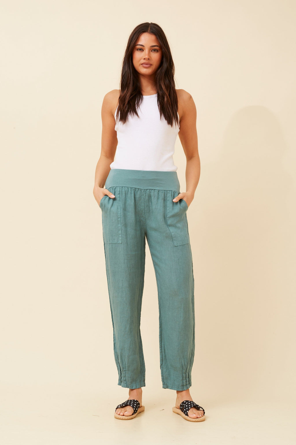 Model wearing Roma Linen Pants with a white tank top and comfortable sandals, showcasing style and elegance.