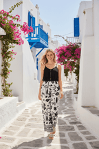 Woman wearing Bahama Pants styled with a black top in a picturesque street lined with flowers.