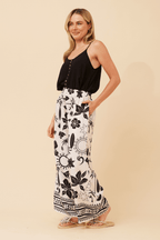 Model wearing Bahama Pants, featuring a cream base with black floral prints and a relaxed wide leg silhouette.