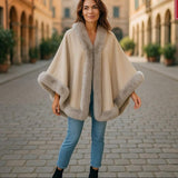 Stylish woman wearing a Jumbo Cape with faux fur trim, showcasing soft polyester design in an elegant outdoor setting.