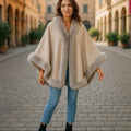 Stylish woman wearing a Jumbo Cape with faux fur trim, showcasing soft polyester design in an elegant outdoor setting.