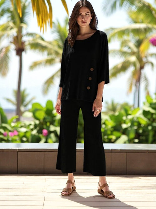 Model showcasing ATN Crop Pants with a stylish black top amidst a tropical backdrop, perfect for casual outings.