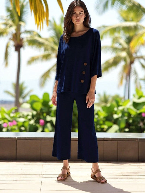 Model wearing ATN Crop Pants with a navy top in a tropical setting, featuring a drawstring waist and wide legs.