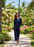 Model wearing ATN Crop Pants in navy, strolling through a tropical garden with palm trees and flowers.