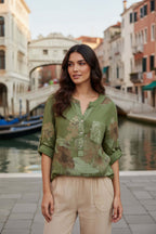 Model wearing WL Amedea Sequin Pocket top in green linen by Wednesday Lulu against a scenic Venetian backdrop.