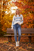 Model wearing a Stripe Crop Jumper with cream, beige, and blue stripes, paired with jeans in a vibrant autumn setting.