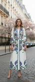 Model wearing a Blooming Dress with floral details, standing on a street adorned with cherry blossoms.