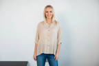 Model wearing Bishop Blouse Beige with button details and relaxed fit, paired with blue jeans against a neutral background.
