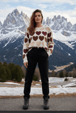A model wearing the Agatha Multi Heart Jumper with heart motifs, set against a snowy mountain backdrop.
