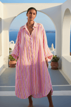 Model wearing Carlotta Shirt Dress in pink and orange stripes, showcasing a relaxed summer style by the beach.