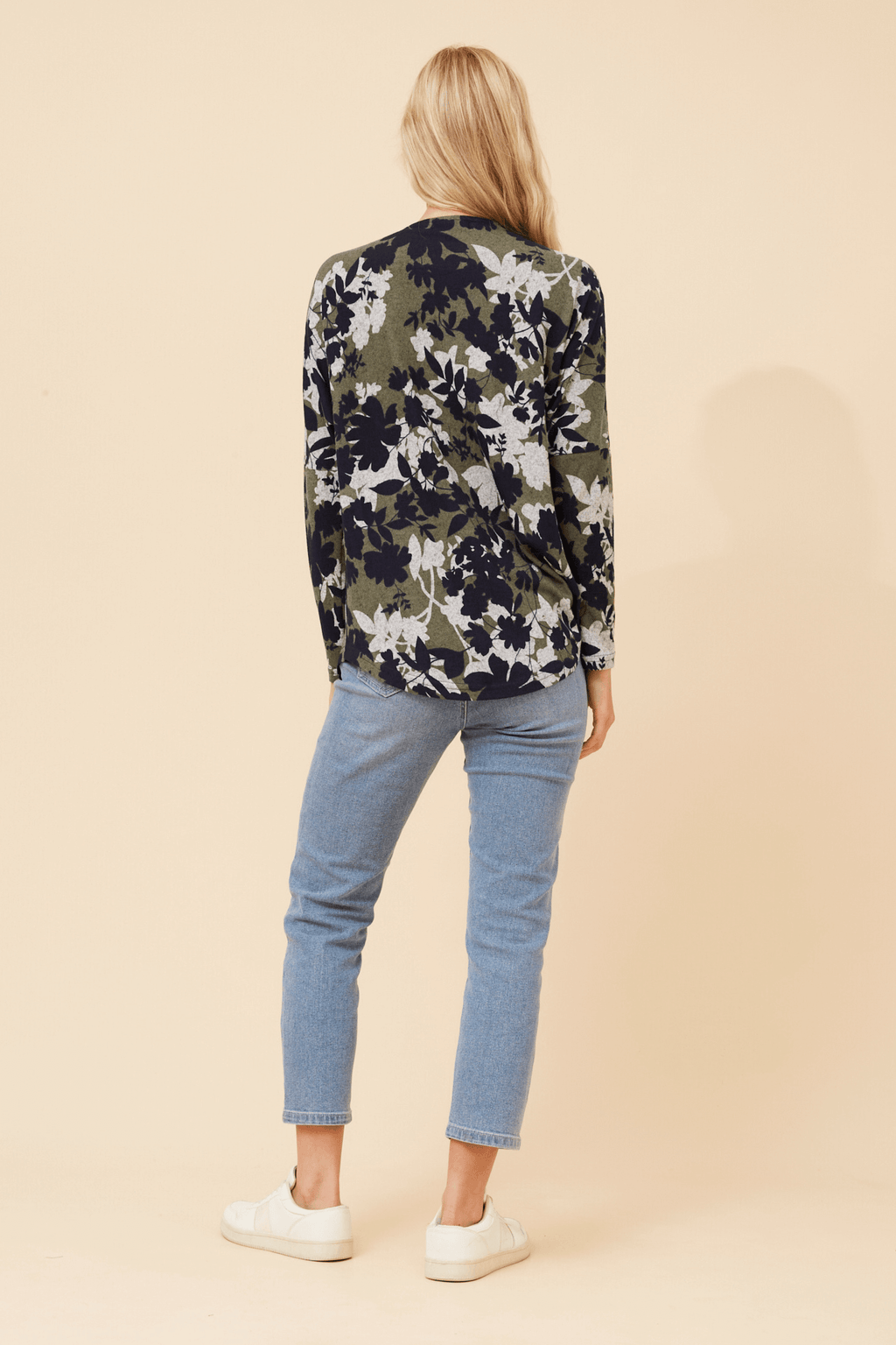 A woman wearing the Valery Zip Top, featuring a floral design, paired with light blue jeans.