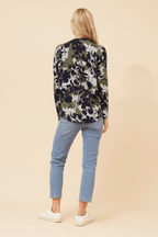 A woman wearing the Valery Zip Top, featuring a floral design, paired with light blue jeans.