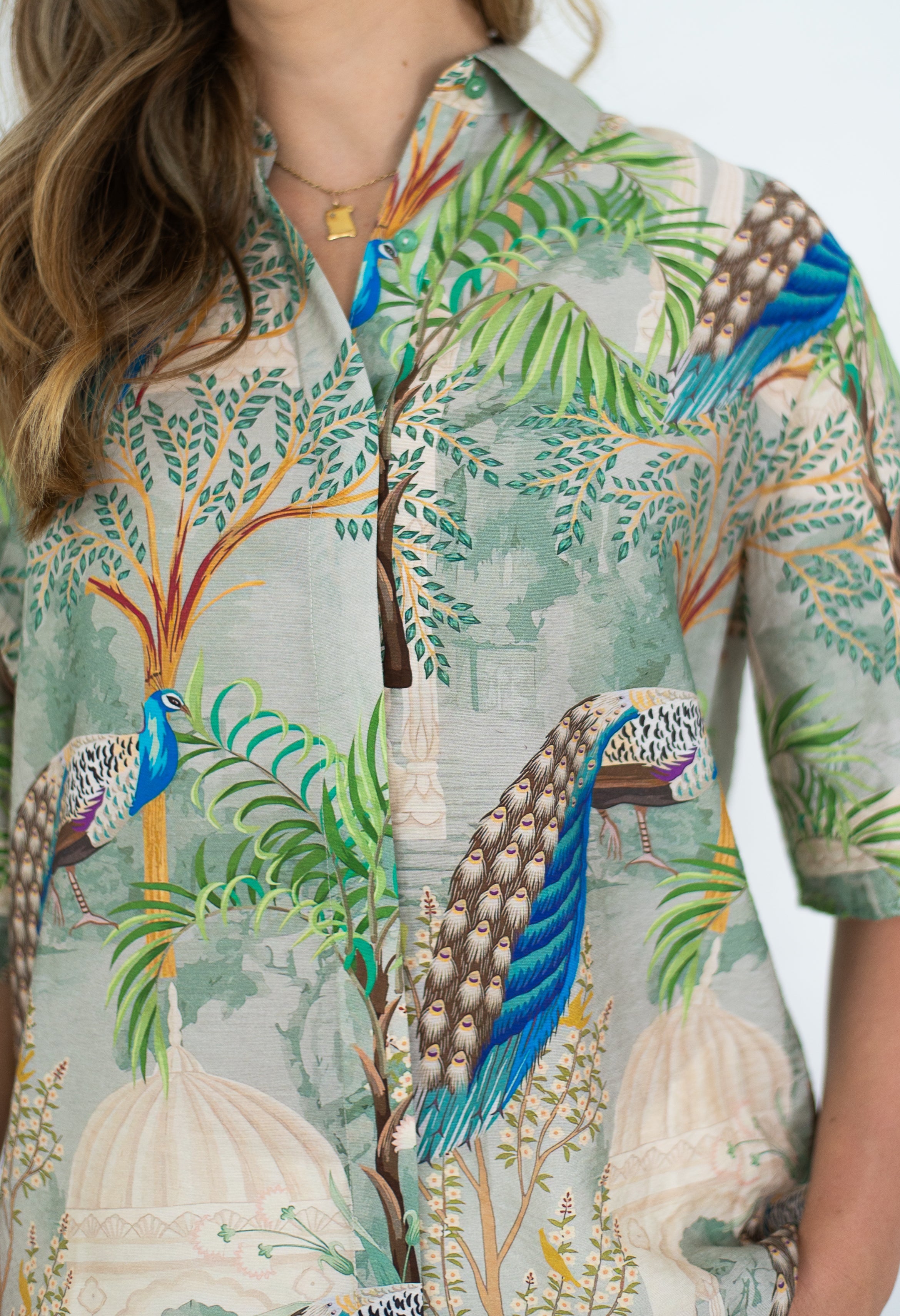 Woman wearing Peacock in Palace shirt featuring vibrant peacock print and lush greenery.