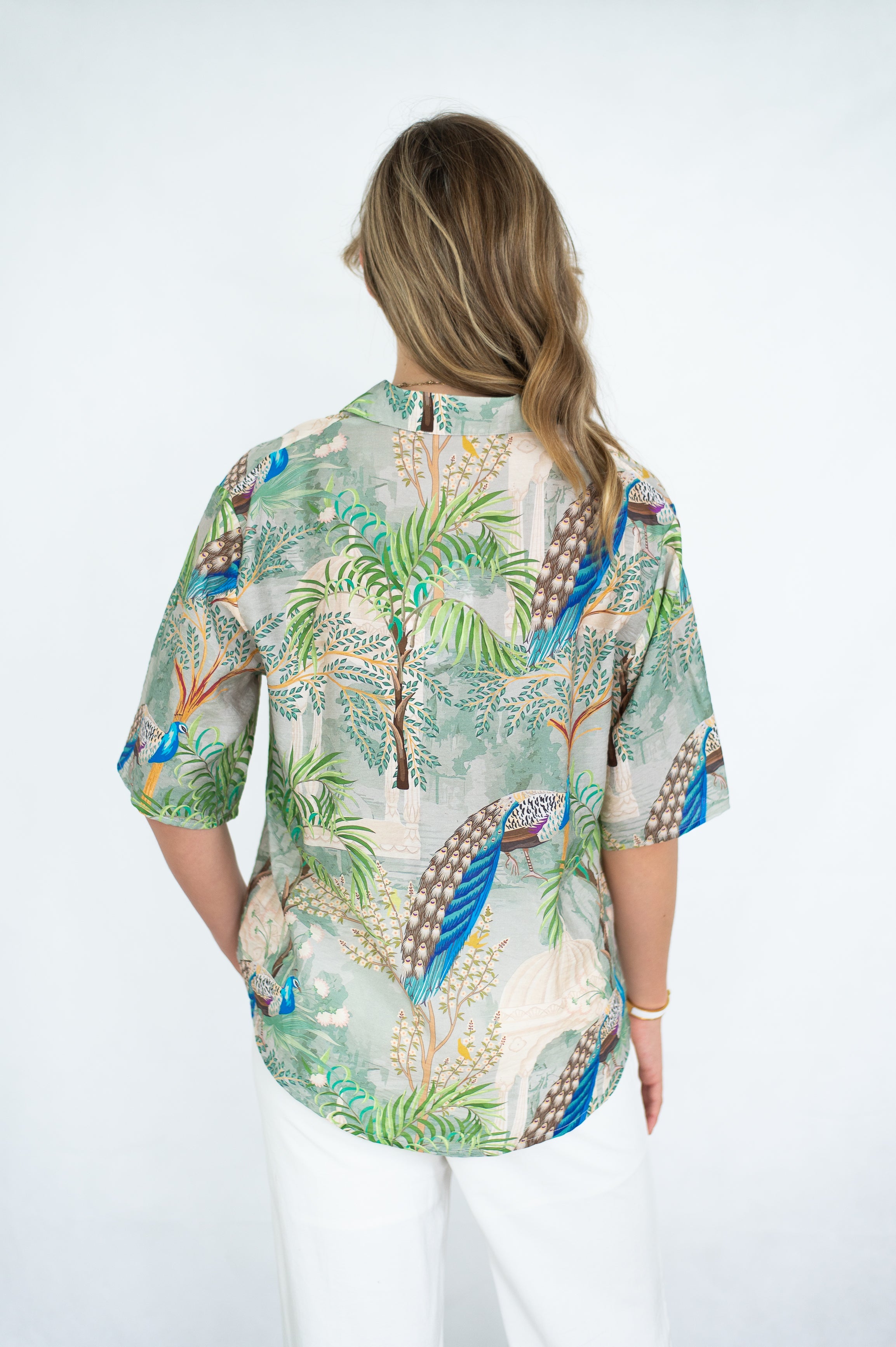 Back view of a woman wearing the Peacock in Palace shirt with vibrant jungle print and short sleeves.