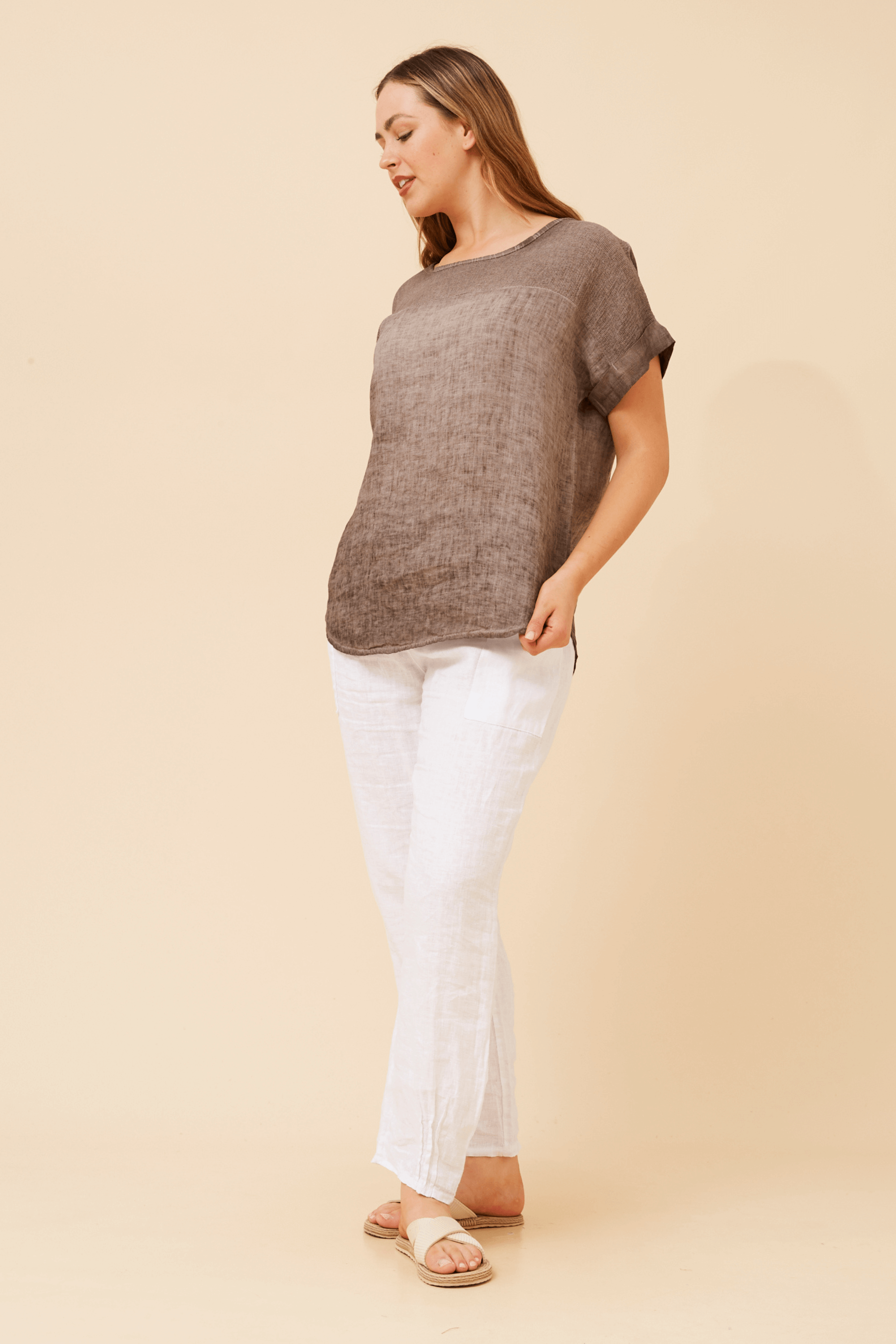 Woman wearing the Angelica Short sleeve chocolate top with white pants, showcasing its elegant style and comfort.