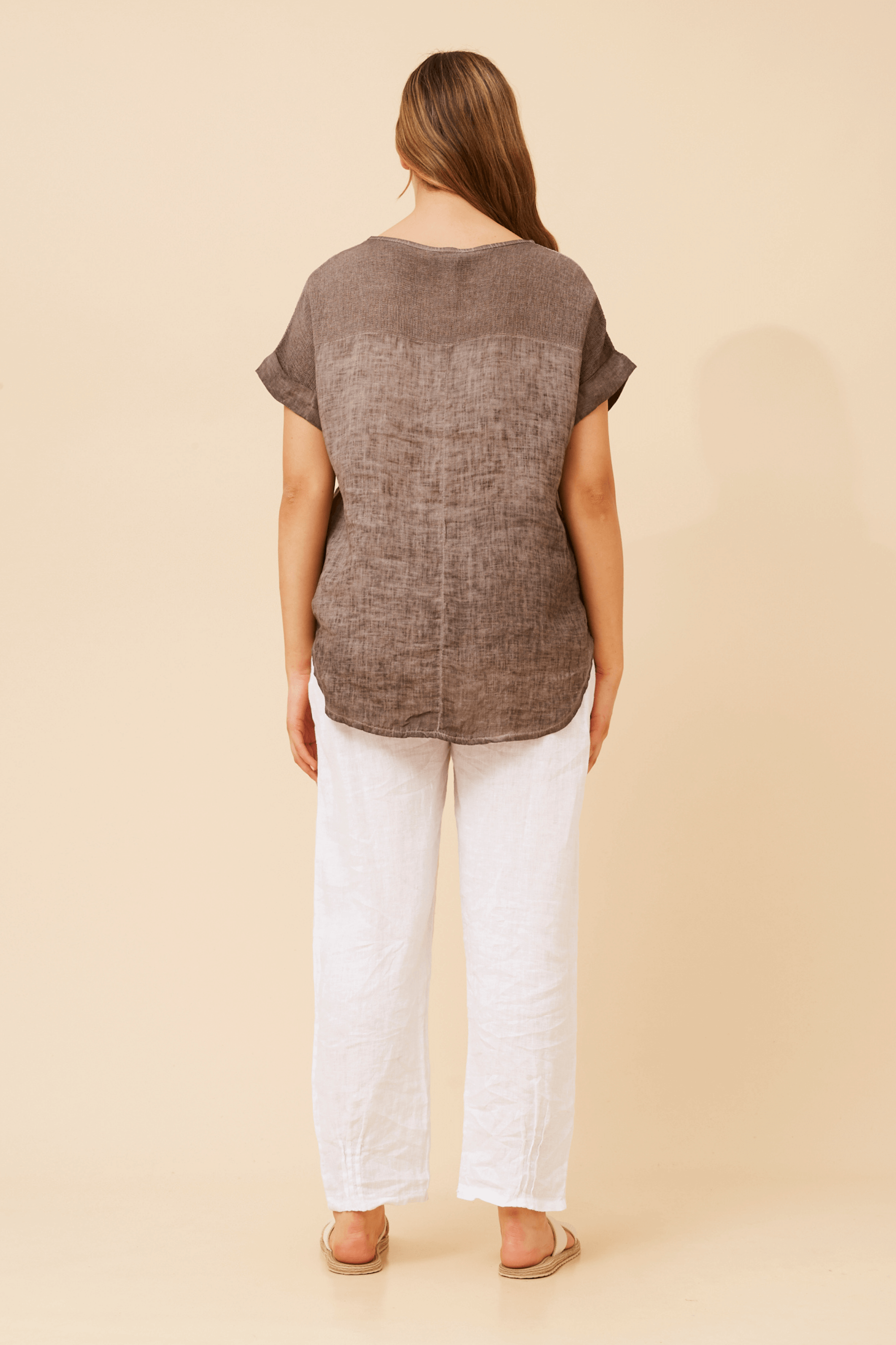 Back view of a model wearing the Angelica Short sleeve chocolate top paired with white linen pants.