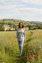 Model wearing the Leonor Cat Zip Top walking through a vibrant flower field with scenic hills in the background.
