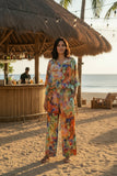 Model showcasing Oriental Digital Pants beside a beach bar in a colorful, relaxed outfit.