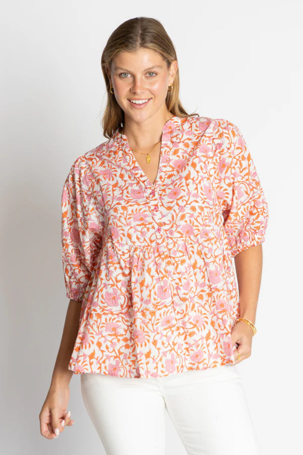Model wearing a pink floral Michigan Top with a relaxed fit and V-neckline, styled with white pants.