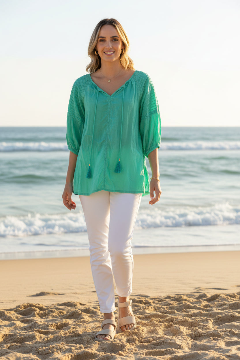 Woman in a Celeste Top walking on the beach, enjoying warm weather in a relaxed fit, vibrant green color.