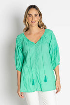 Woman wearing the Celeste Top in vibrant green, showcasing its relaxed fit and delicate ties.