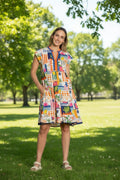 Model wearing the Lyra Tiered Dress in a vibrant patchwork print against a sunny park backdrop.