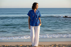 Model wearing Lulalife Sardine Top on the beach, paired with white pants, enjoying the ocean view.
