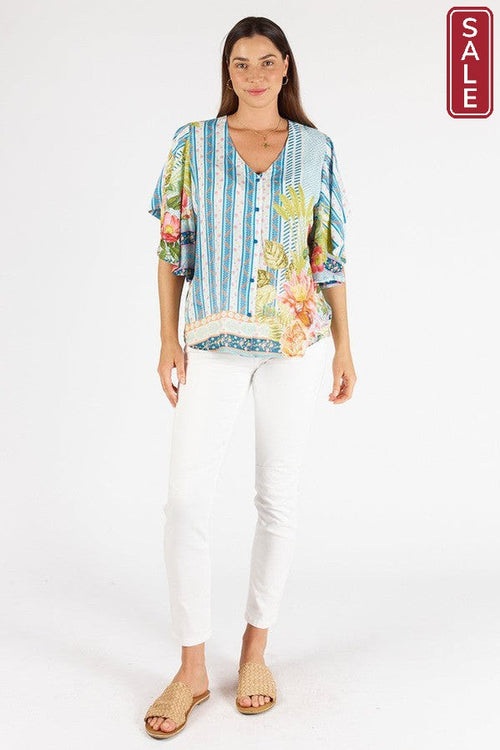 Model wearing Bahama Flutter Top Lagoon with floral design and V neck, paired with white pants. Perfect for warm weather!