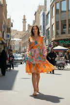 Model walking in the city wearing the vibrant Quintana Dress, showcasing floral patterns and a V-neckline.