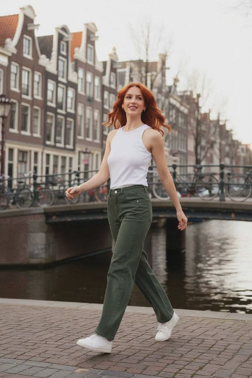 Model wearing Annika Barrel Jean in khaki with a white top, walking by a canal in a stylish urban setting.