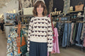 Freja Love Heart Jumper on model surrounded by stylish clothing in a chic boutique.