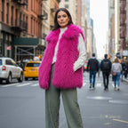 Mongolian Vest in bright pink faux fur with side pockets, modeled on city street backdrop.