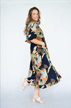 Model wearing Raya Dress with a scoop neck and tiered skirt, featuring navy leaves print and pockets.