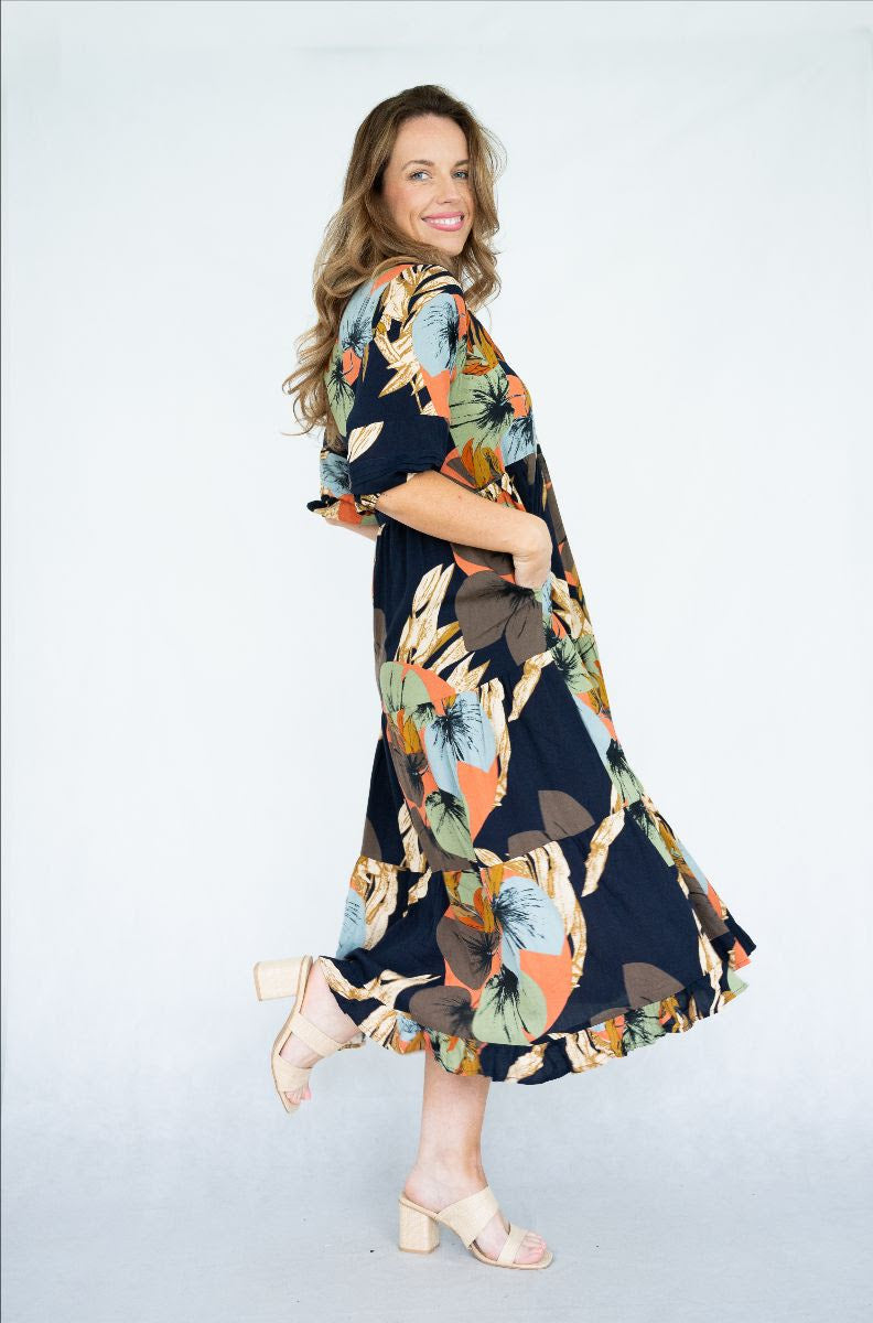 Model wearing Raya Dress with a scoop neck and tiered skirt, featuring navy leaves print and pockets.