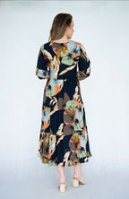 Back view of woman wearing Raya Dress with scoop neck and tiered skirt in navy leaves print.