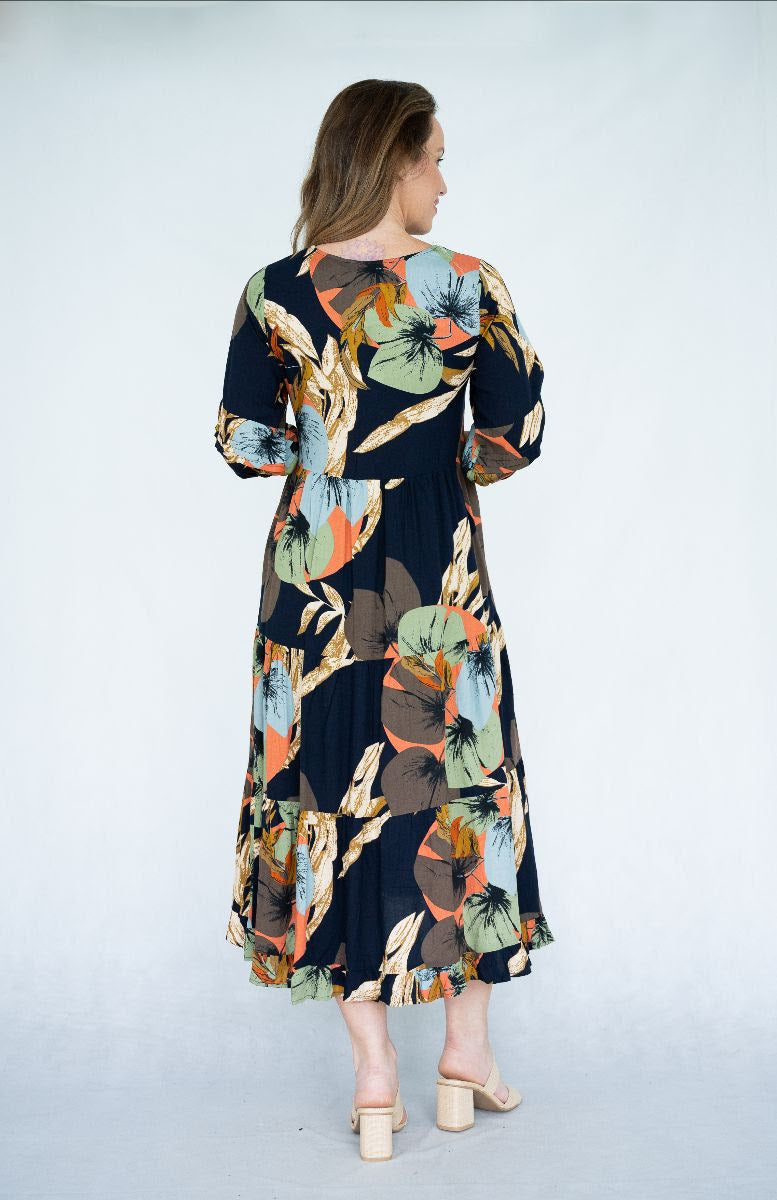Back view of woman wearing Raya Dress with scoop neck and tiered skirt in navy leaves print.