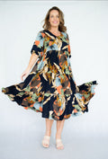 Model twirling in a vibrant Raya Dress featuring a scoop neck, tiered skirt, and navy leaves print.