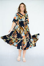 Model twirling in a vibrant Raya Dress featuring a scoop neck, tiered skirt, and navy leaves print.