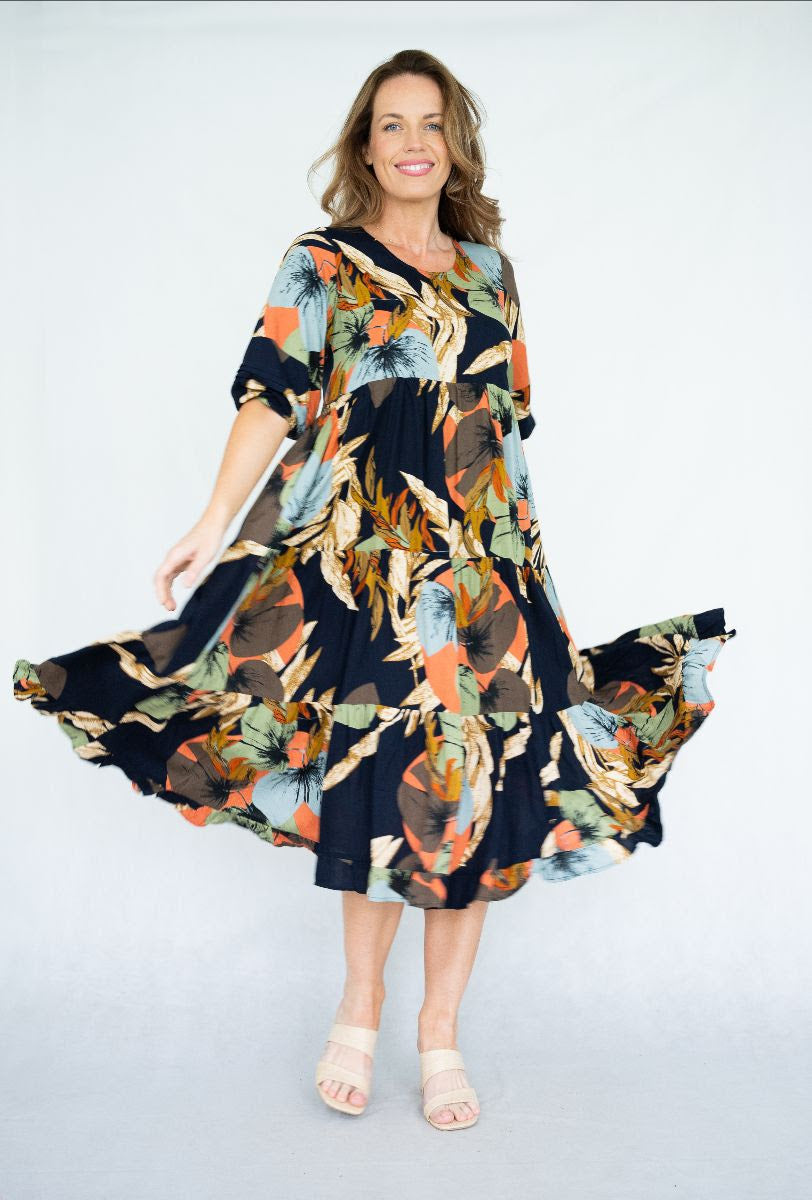 Model twirling in a vibrant Raya Dress featuring a scoop neck, tiered skirt, and navy leaves print.